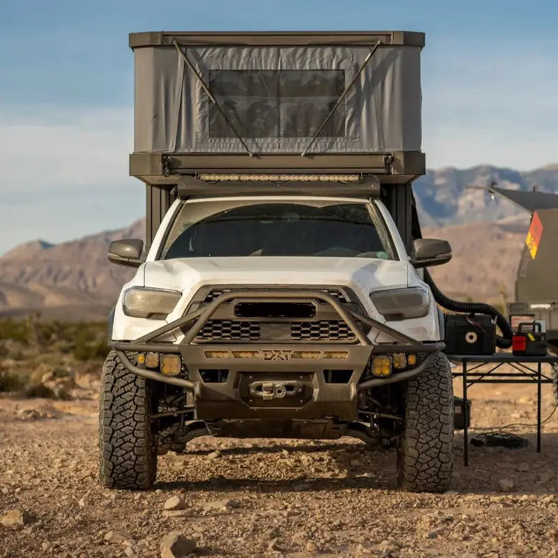 White 2016-2023 Toyota Tacoma equipped with DRT Hybrid Front Bumper, rooftop tent, and off-road accessories in a desert setting.