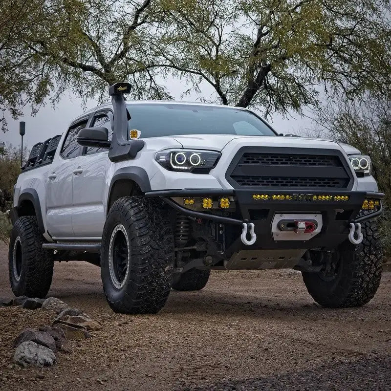 White 2016-2023 Toyota Tacoma with DRT Hybrid Front Bumper, off-road lights, and winch setup in a rugged outdoor environment.