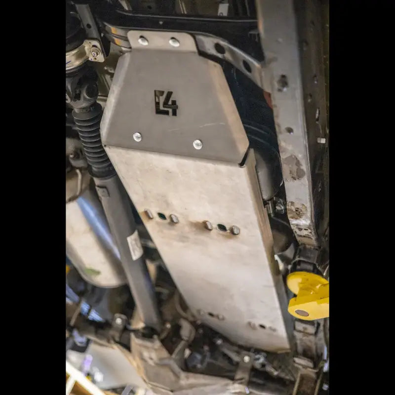 Close-up view of a Tacoma fuel tank skid plate mounted under a vehicle, showcasing bolt-on steel design for 2005-2015 models.