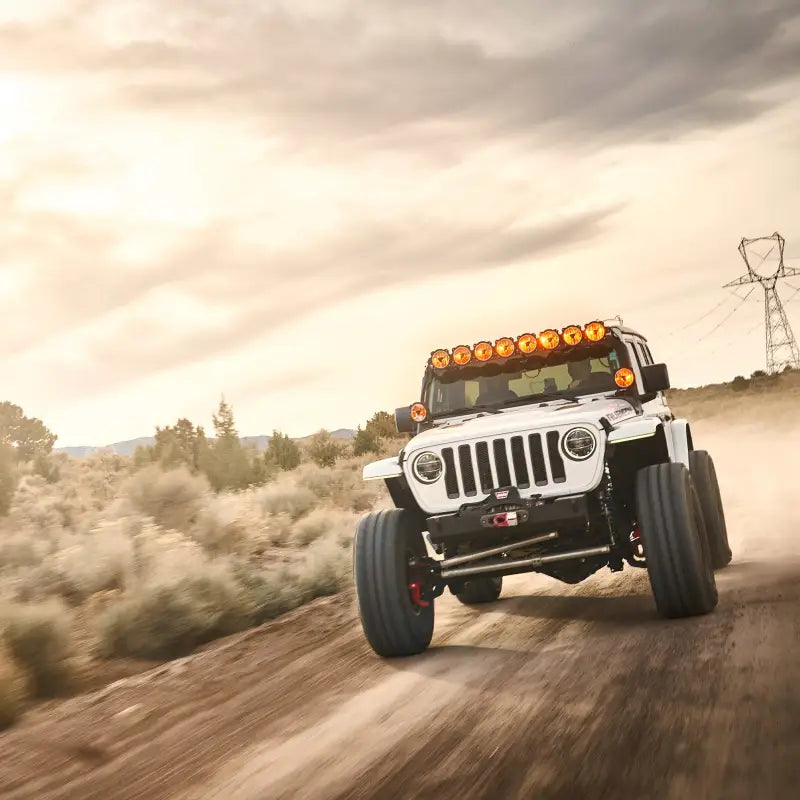 White Jeep with Gravity® Titan™ 6-inch LED lights, driving through off-road terrain with amber illumination and wide visibility.