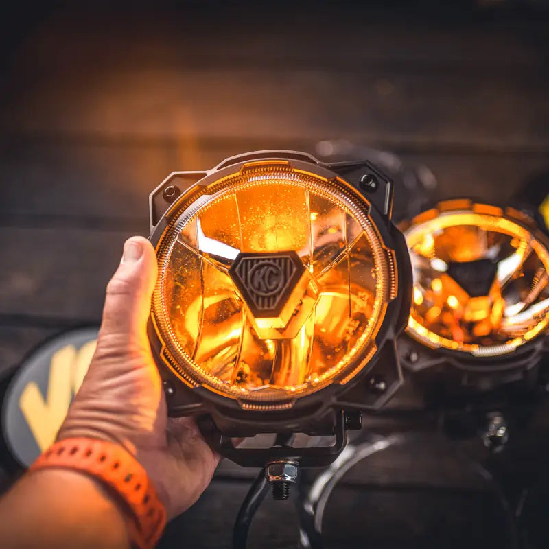 Hand holding Gravity® Titan™ 6-inch LED off-road light with amber illumination, highlighting its high-beam power and rugged design.