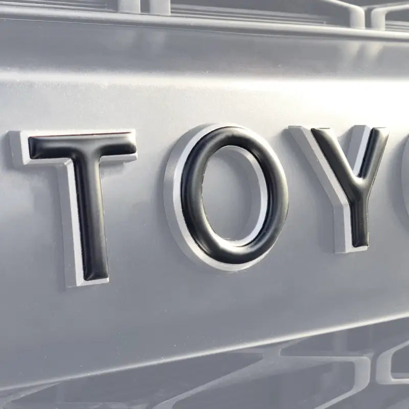 Close-up of grille letter overlays for Toyota 4Runner 2010-2024 in a silver finish, enhancing vehicle decor.