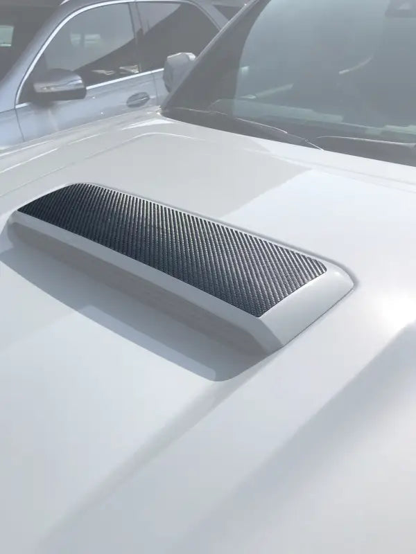 Hood scoop accent overlay in carbon fiber texture installed on a white 2016-2023 Toyota Tacoma, enhancing the vehicle's exterior design.