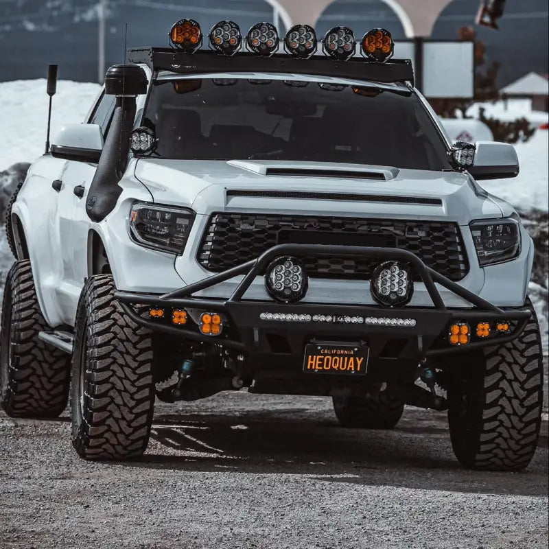 White Toyota Tundra equipped with hybrid front bumper, LED lights, and large off-road tires, suitable for 2014-2021 models.