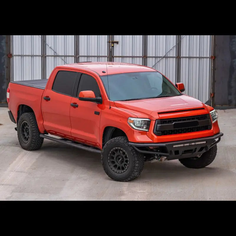 Side view of orange Toyota Tundra with hybrid front bumper, LED bar, and off-road tires, suitable for 2014-2021 models.