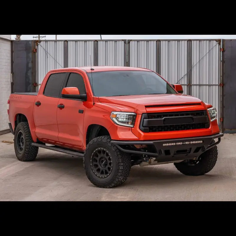 Orange Toyota Tundra with hybrid front bumper, LED bar, and off-road tires, suitable for 2014-2021 models, parked in front of a gate.