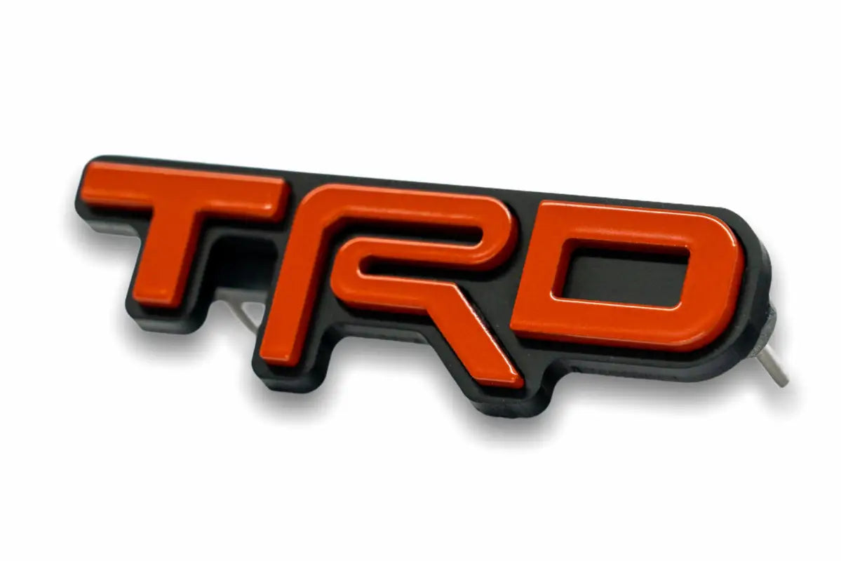 Orange and black TRD emblem logo grille badge for route protection on Toyota vehicles
