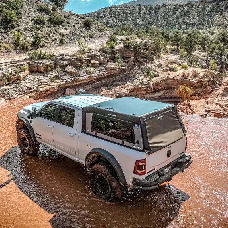 MR - Full-Size 6.4' Bed air-topper shell on a white truck crossing a rocky stream, emphasizing its durability and off-road capability.