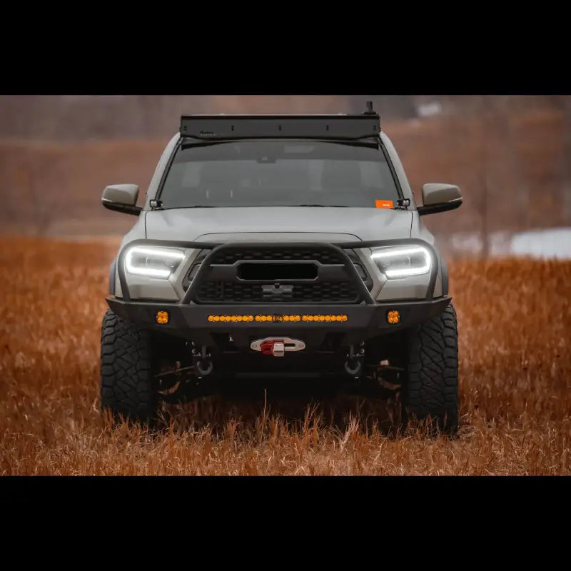 Close-up front view of a 3rd Gen Toyota Tacoma with Overland Front Bumper, winch, and light bar in a field. Fits 2016+ models.