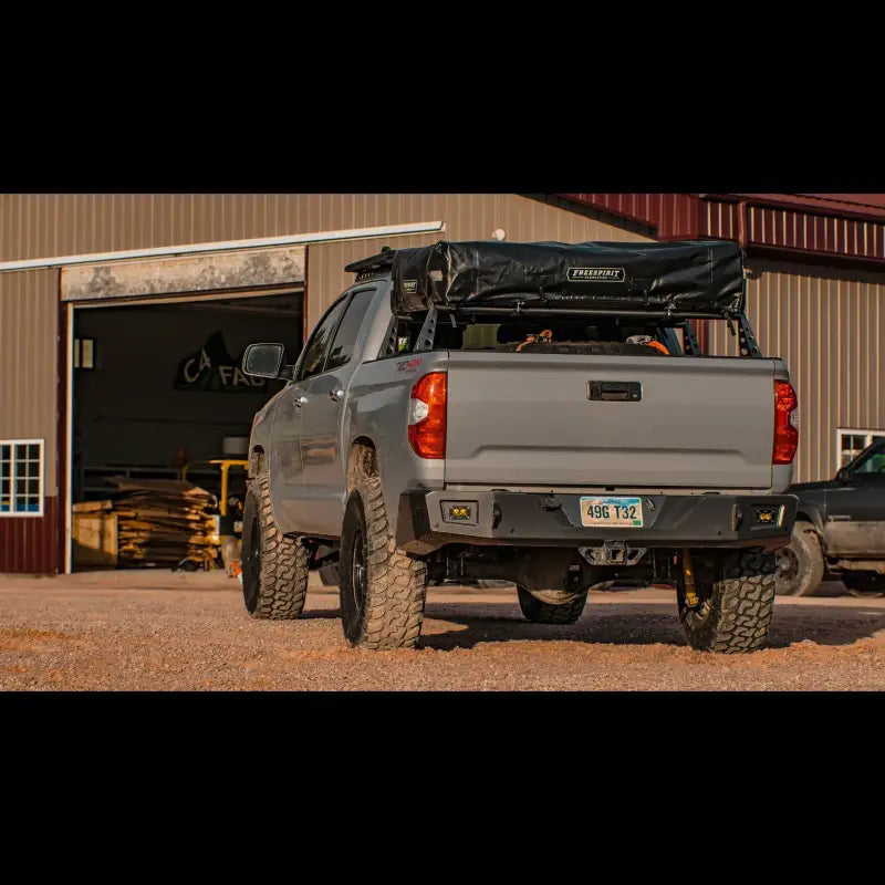 2014-2021 Tundra with Overland Rear Bumper, steel construction, light cutouts, and OE hitch fit, parked near a workshop.