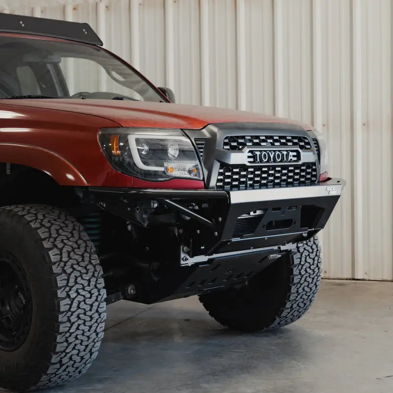 Angled front view of a red Toyota Tacoma showcasing the Rock Runner modular front bumper with integrated skid plate.