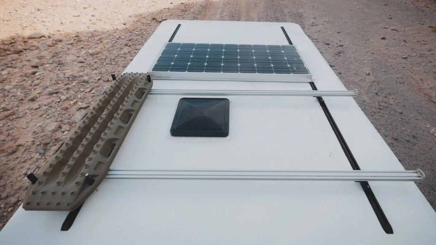 Top-down view of a camper roof with Roof Track Load Bars, carrying a solar panel and recovery boards for outdoor adventures.