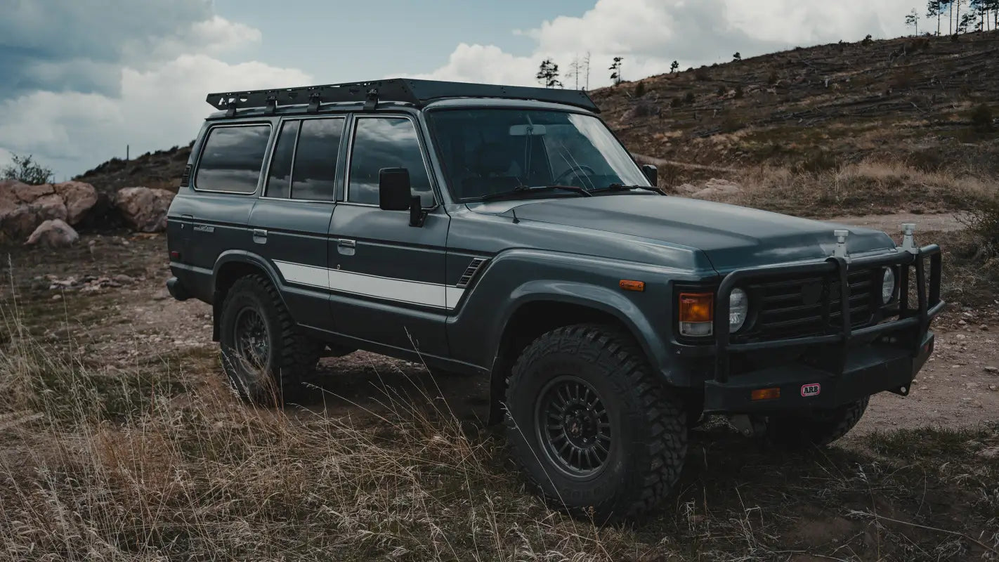 Toyota Land Cruiser 60 Series with a rugged roof rack parked in a mountainous terrain, ideal for outdoor gear transport and off-road use.