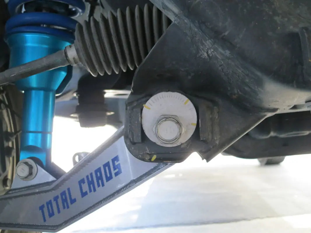Installed Total Chaos cam tab gussets on a vehicle's lower control arm, ensuring secure alignment and enhanced suspension durability.